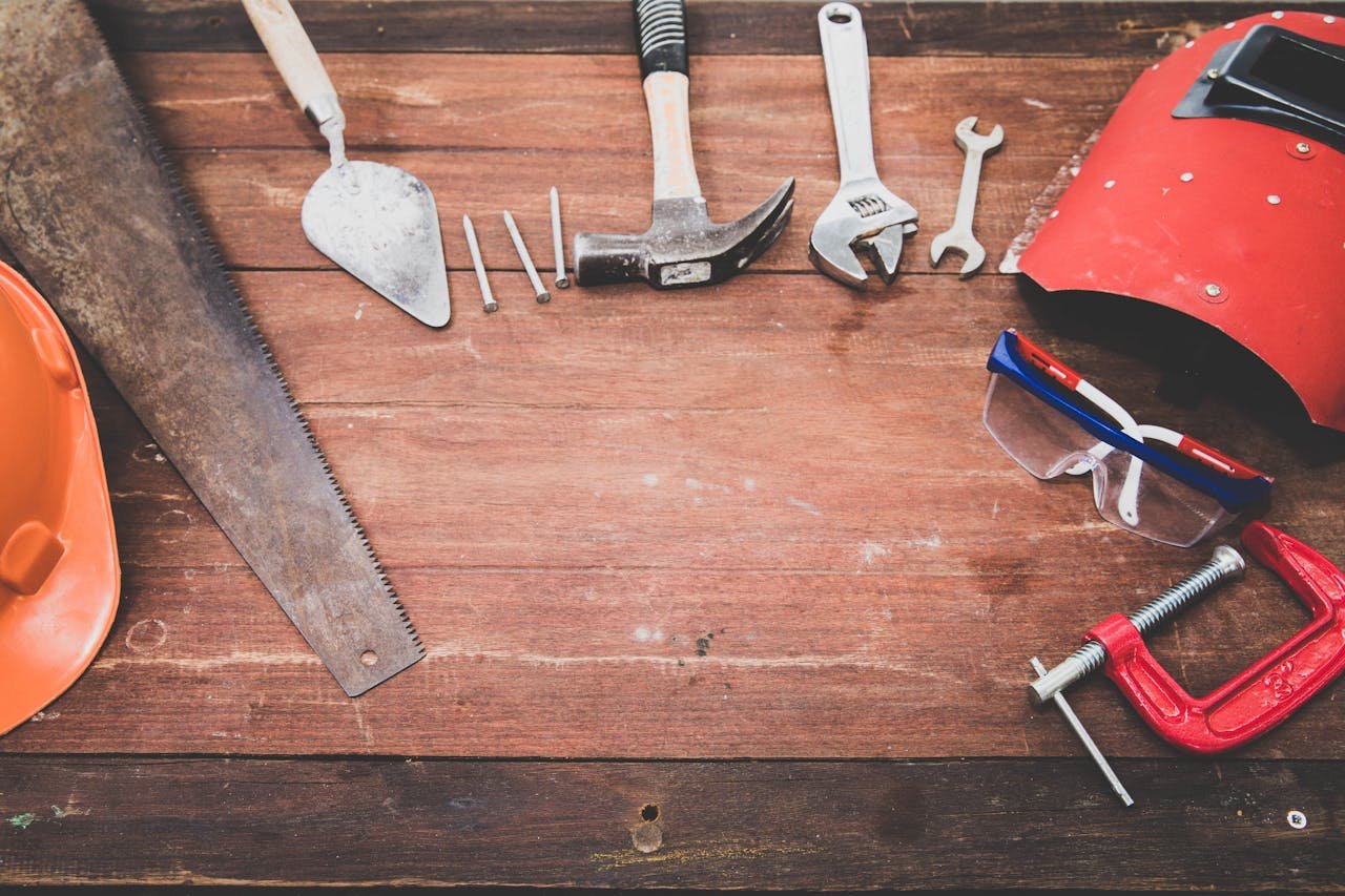 about-us Flat lay of various workshop tools on a rustic wooden table, showcasing DIY essentials.